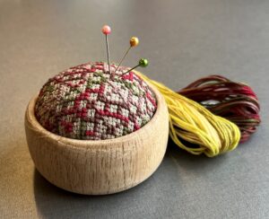 Kit med hånddrejet trænålepude og korsstingsbroderi.