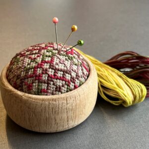 Kit med hånddrejet trænålepude og korsstingsbroderi.