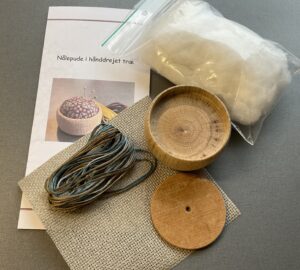 Kit med hånddrejet trænålepude og korsstingsbroderi.